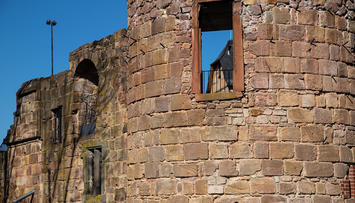 Steinruinen eines alten Rundbaus mit einem großen offenen Fenster und blauem Himmel im Hintergrund; perfekt für „Wandern Wetteraukreis“, wobei durch die Fensteröffnung ein weiteres Bauwerk zu sehen ist.