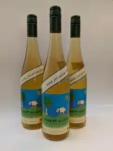 Drei Flaschen hellgelber Sekt mit blauen Etiketten, auf denen ein Comic-Baum, ein Schaf und eine Sonne abgebildet sind. Perfekt für Wanderungen im Wetteraukreis oder zum Erkunden der Wanderwege von Bad Vilbel. Auf dem Etikett steht „...eine prickelnde Sache“ und „WINGERT GLÜCK“; die Flaschen haben schwarze Schraubverschlüsse.